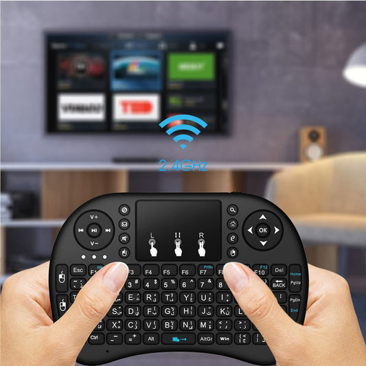 Hand holding a wireless keyboard in front of a TV displaying a streaming interface.