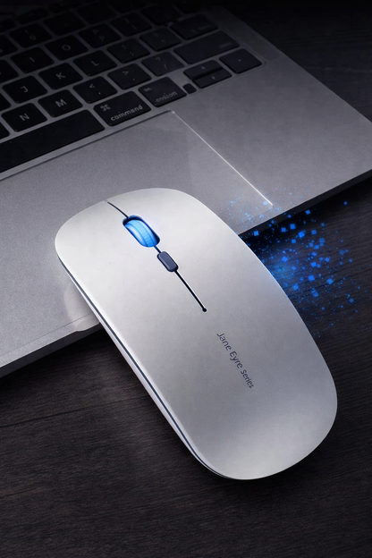 White computer mouse with blue light on a dark surface next to a laptop